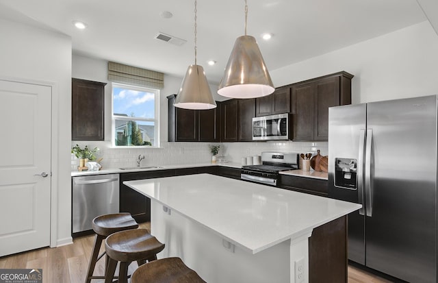 kitchen featuring sink, decorative backsplash, light hardwood / wood-style floors, a kitchen island, and stainless steel appliances