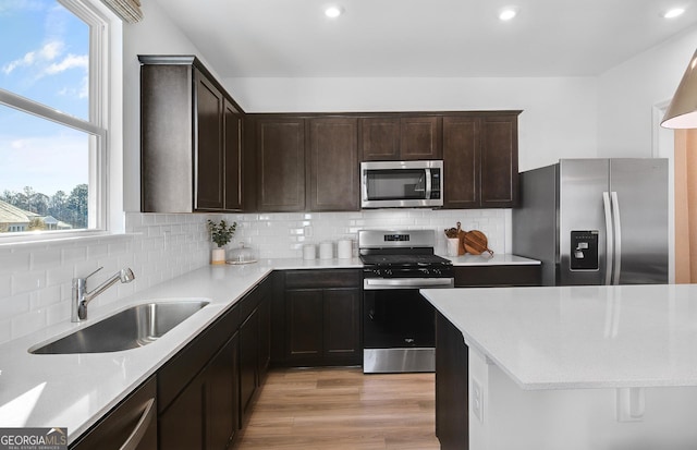 kitchen with sink, a healthy amount of sunlight, stainless steel appliances, tasteful backsplash, and light hardwood / wood-style floors