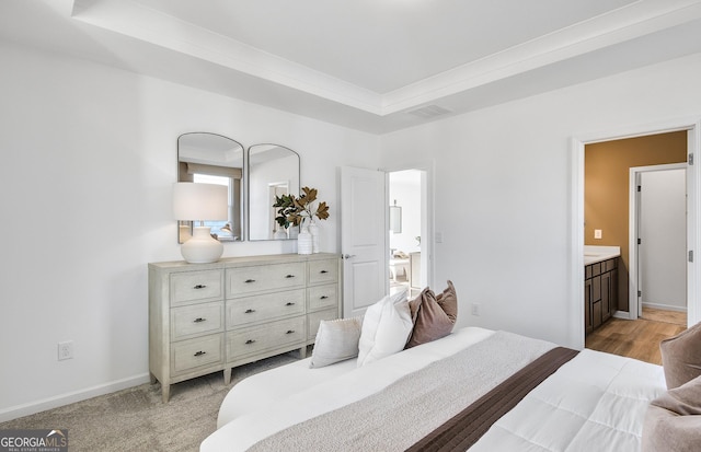 bedroom with a tray ceiling, ensuite bath, and ornamental molding