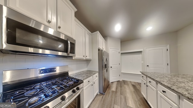 kitchen with light hardwood / wood-style floors, light stone counters, white cabinetry, and appliances with stainless steel finishes