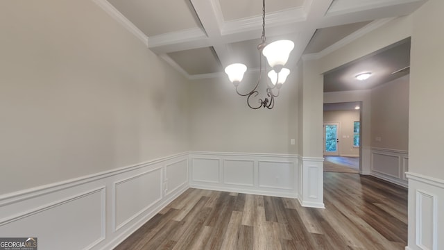 unfurnished room with coffered ceiling, beamed ceiling, a notable chandelier, light wood-type flooring, and ornamental molding