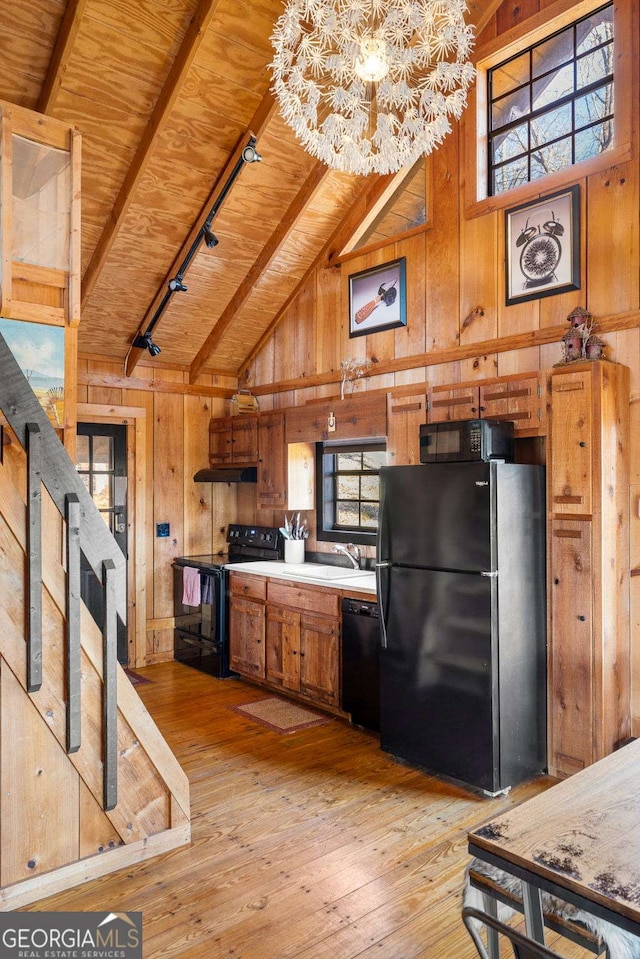 kitchen featuring rail lighting, an inviting chandelier, light hardwood / wood-style flooring, wooden walls, and black appliances