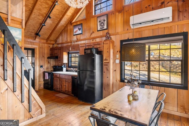 kitchen with black appliances, a wall mounted AC, light hardwood / wood-style flooring, and wood walls