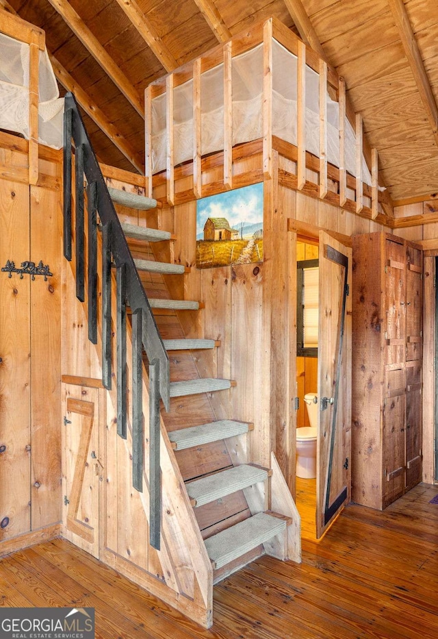 stairs featuring hardwood / wood-style floors, vaulted ceiling with beams, wooden ceiling, and wood walls