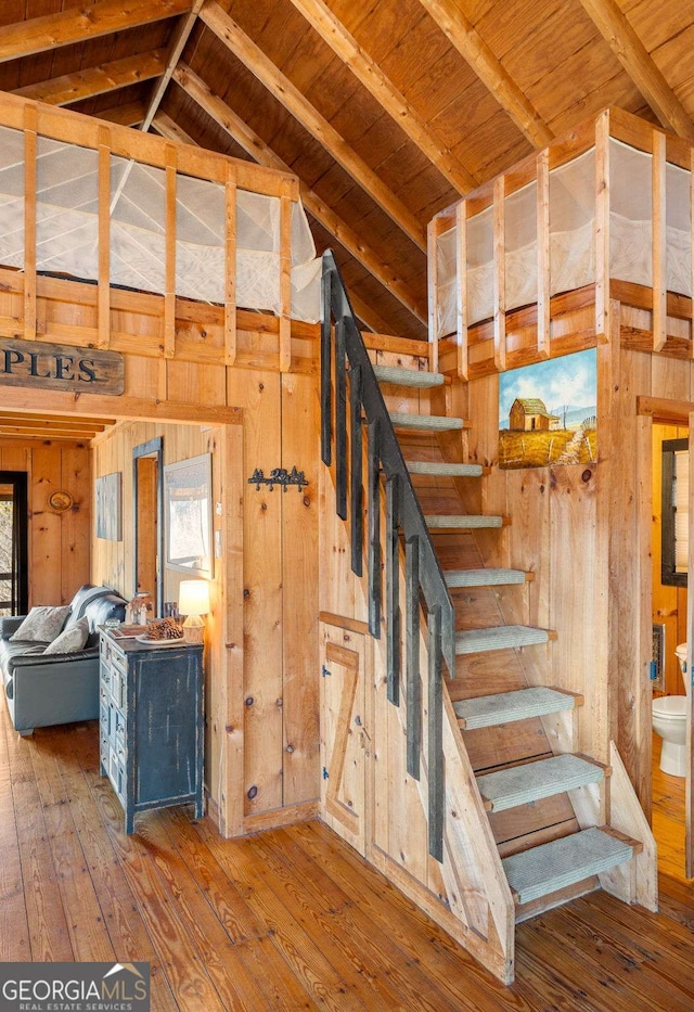 stairs with wood-type flooring, vaulted ceiling with beams, wood ceiling, and wood walls