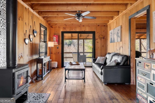 interior space with beam ceiling, a wood stove, wood walls, and hardwood / wood-style floors