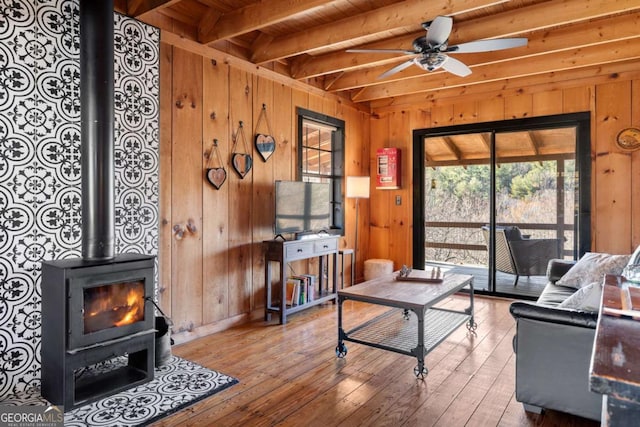 living room with a wood stove, ceiling fan, wooden walls, and wood ceiling