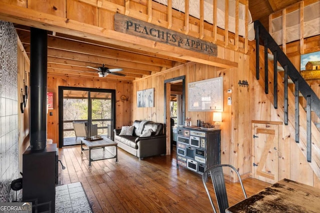 living room with ceiling fan, wooden walls, a wood stove, hardwood / wood-style flooring, and beam ceiling