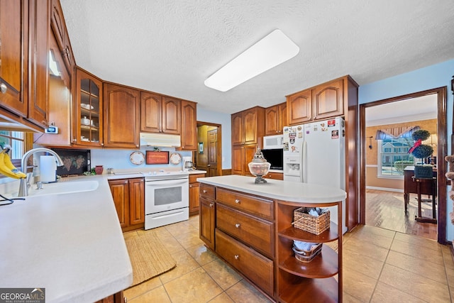 kitchen with sink, a kitchen island, a textured ceiling, white appliances, and light tile patterned floors