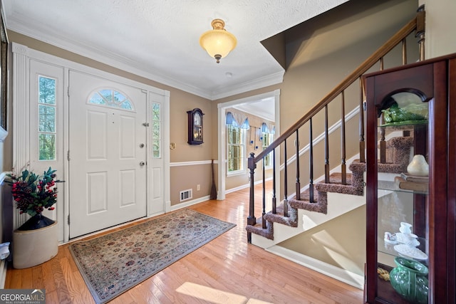 entryway featuring a textured ceiling, light hardwood / wood-style floors, crown molding, and a wealth of natural light