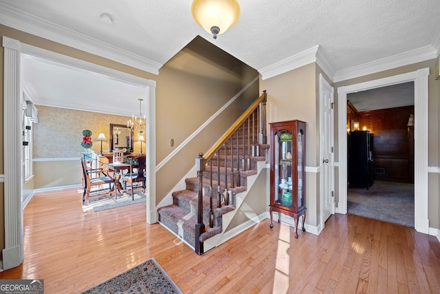 stairway with crown molding, wood-type flooring, a textured ceiling, and a notable chandelier