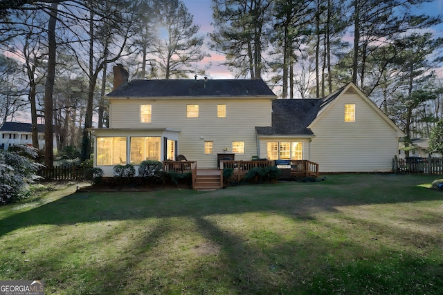 back house at dusk featuring a sunroom, a deck, and a lawn