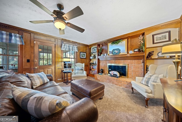 carpeted living room featuring ornamental molding, a textured ceiling, ceiling fan, wooden walls, and a fireplace