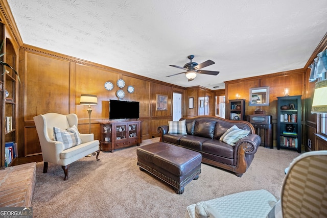 carpeted living room with ceiling fan, crown molding, and wooden walls