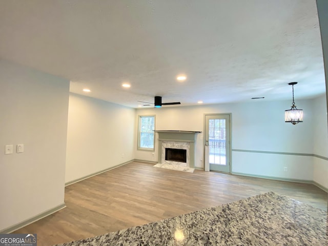 unfurnished living room featuring a high end fireplace, ceiling fan, and light wood-type flooring