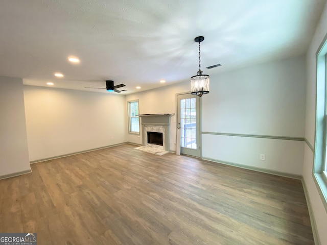 unfurnished living room featuring hardwood / wood-style flooring, a fireplace, and ceiling fan with notable chandelier