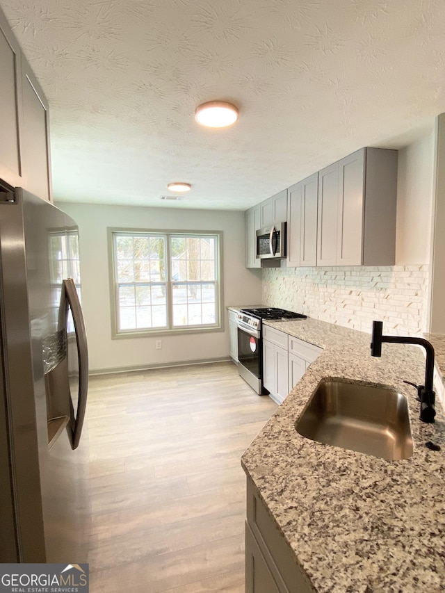 kitchen with sink, gray cabinetry, stainless steel appliances, light stone countertops, and decorative backsplash