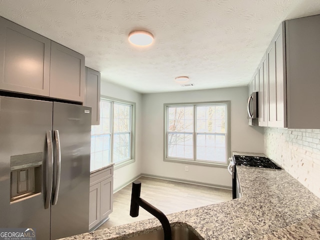 kitchen featuring light stone counters, stainless steel appliances, decorative backsplash, and gray cabinetry