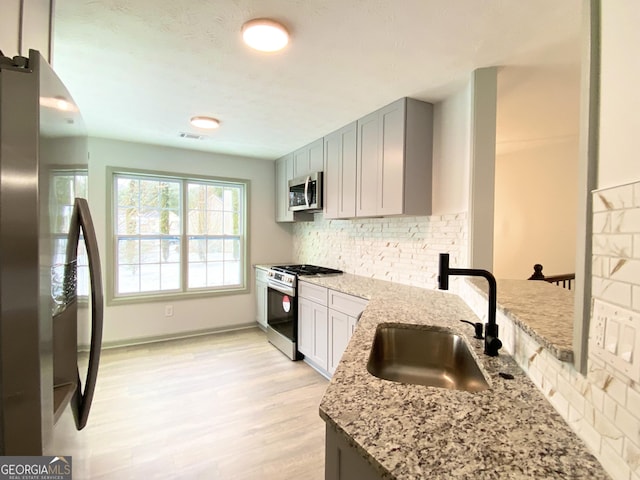 kitchen featuring stainless steel appliances, tasteful backsplash, light stone countertops, and sink