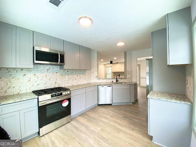 kitchen featuring sink, light hardwood / wood-style flooring, stainless steel appliances, tasteful backsplash, and light stone countertops