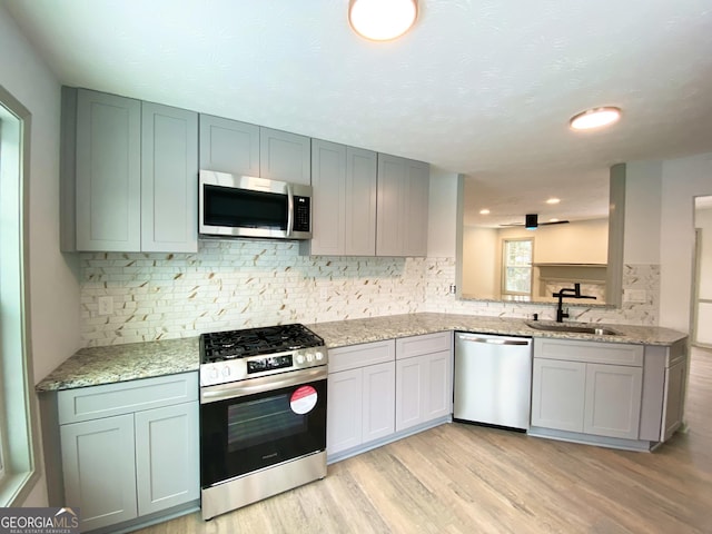 kitchen featuring stainless steel appliances, light stone countertops, sink, and light wood-type flooring