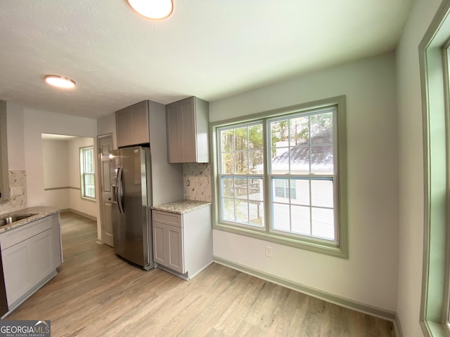 kitchen with gray cabinetry, stainless steel refrigerator with ice dispenser, light stone counters, tasteful backsplash, and light hardwood / wood-style floors