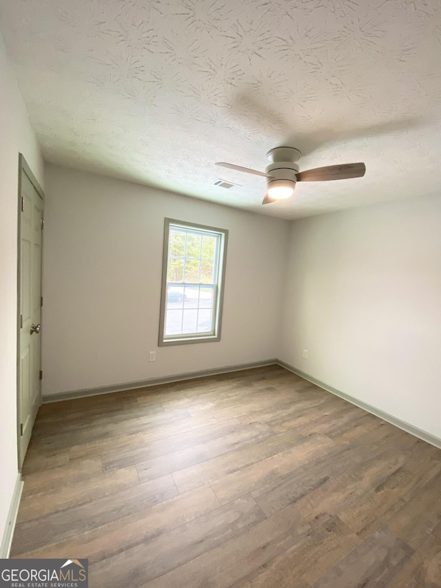 empty room featuring ceiling fan, hardwood / wood-style floors, and a textured ceiling