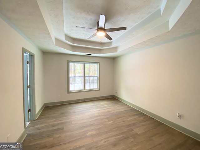 spare room with ceiling fan, wood-type flooring, a raised ceiling, and a textured ceiling