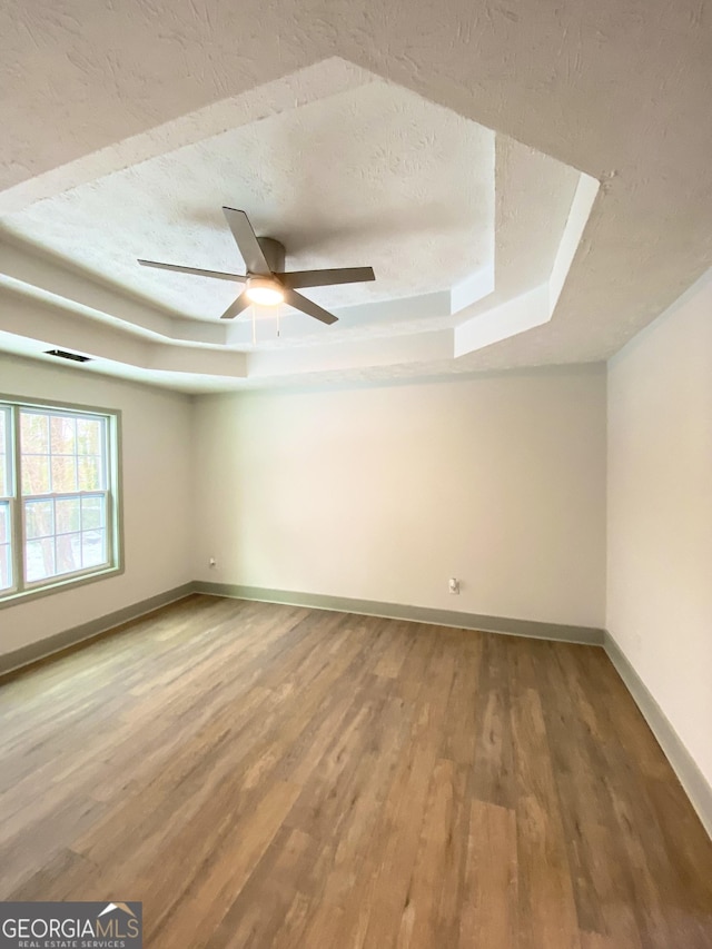 spare room featuring ceiling fan, wood-type flooring, a raised ceiling, and a textured ceiling