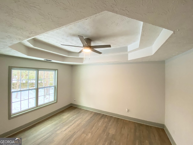 unfurnished room with a raised ceiling, hardwood / wood-style floors, and a textured ceiling