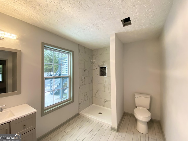 bathroom featuring vanity, tiled shower, a textured ceiling, and toilet