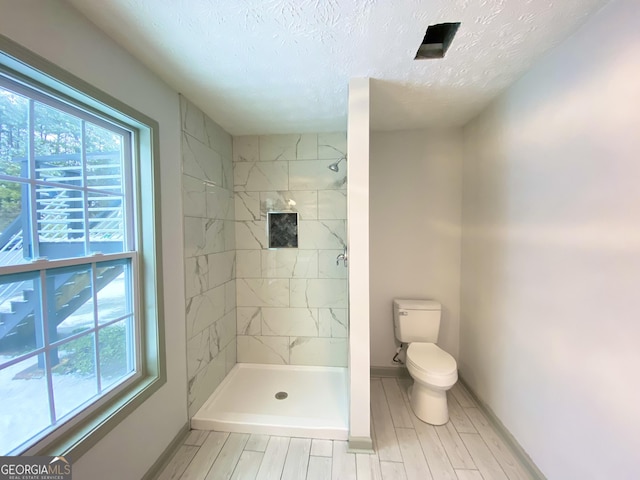 bathroom featuring a textured ceiling, toilet, and tiled shower