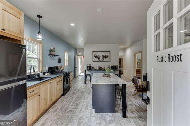 kitchen featuring sink, light brown cabinets, hanging light fixtures, a breakfast bar, and black appliances