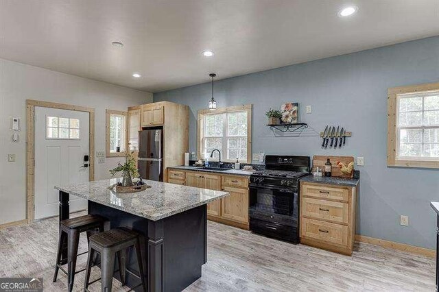 kitchen featuring a kitchen breakfast bar, black range with gas stovetop, sink, stainless steel fridge, and a kitchen island