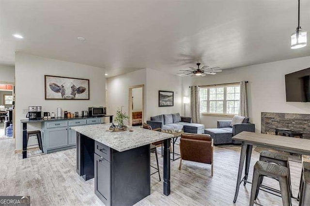 kitchen featuring light stone countertops, light wood-type flooring, a breakfast bar, decorative light fixtures, and a center island