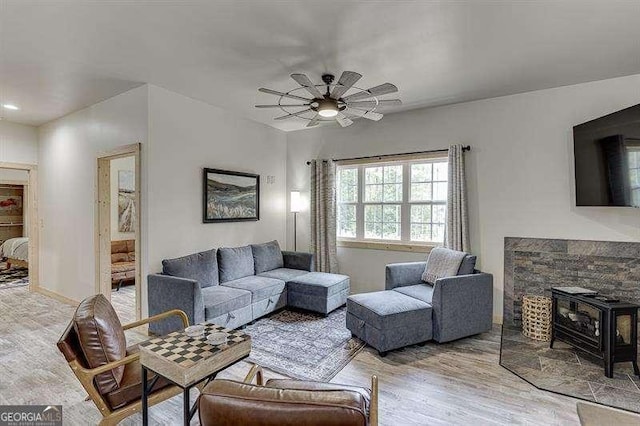 living room with light wood-type flooring, a wood stove, and ceiling fan