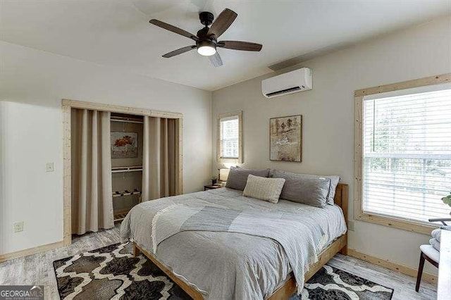 bedroom featuring a wall unit AC, multiple windows, ceiling fan, and light hardwood / wood-style flooring