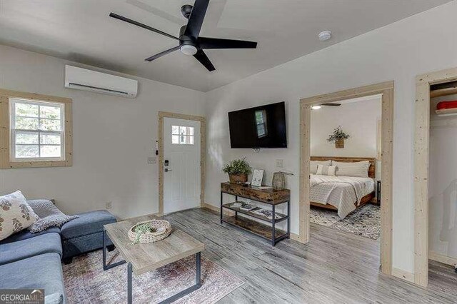 living room featuring a wall mounted AC, ceiling fan, and light hardwood / wood-style flooring