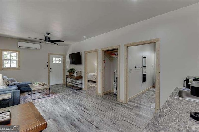 living room with a wall mounted air conditioner, ceiling fan, light wood-type flooring, and sink