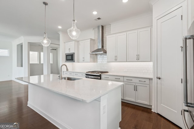 kitchen with wall chimney range hood, sink, a kitchen island with sink, hanging light fixtures, and built in microwave