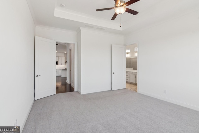 unfurnished bedroom featuring light colored carpet, a tray ceiling, and ensuite bath