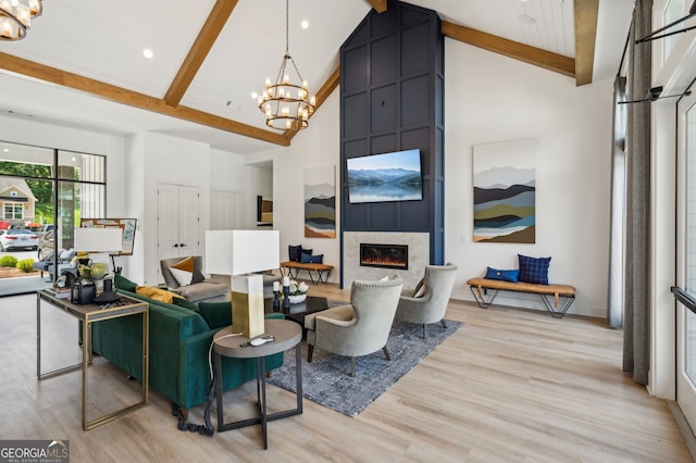 living room featuring beam ceiling, light wood-type flooring, a notable chandelier, and a fireplace