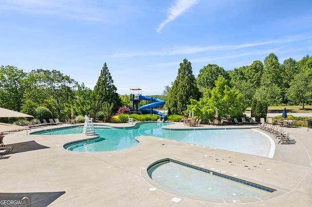 view of swimming pool with a water slide, a patio, and a hot tub