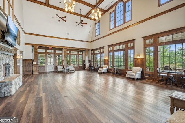 unfurnished living room featuring hardwood / wood-style flooring, a stone fireplace, a towering ceiling, and ornate columns