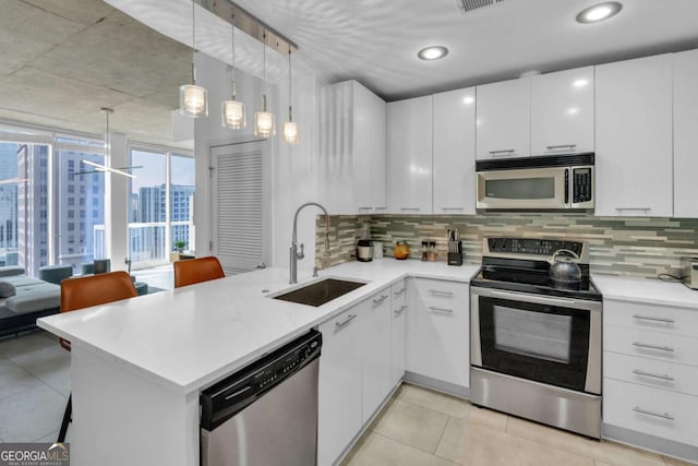 kitchen featuring sink, kitchen peninsula, decorative light fixtures, white cabinetry, and stainless steel appliances