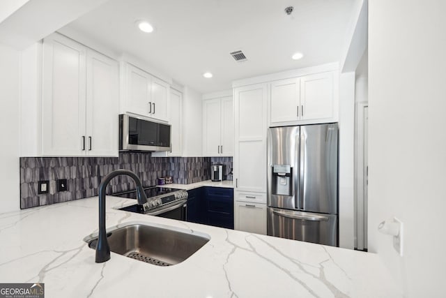 kitchen featuring backsplash, white cabinets, sink, light stone countertops, and appliances with stainless steel finishes