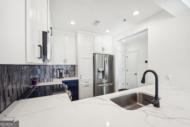 kitchen with light stone countertops, stainless steel refrigerator with ice dispenser, backsplash, sink, and white cabinets