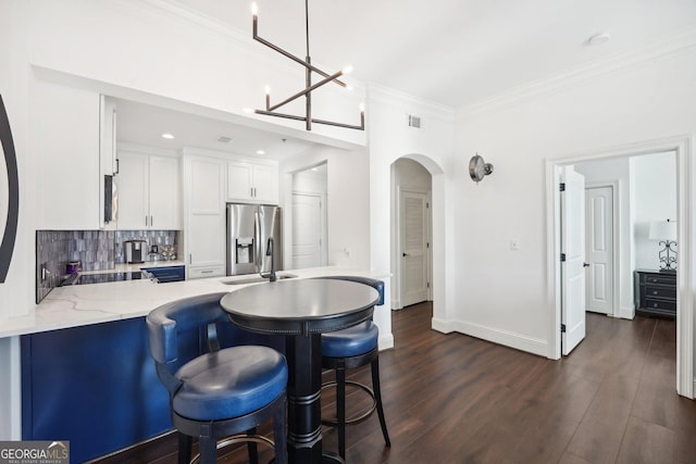 kitchen featuring hanging light fixtures, stainless steel fridge, light stone countertops, white cabinetry, and kitchen peninsula