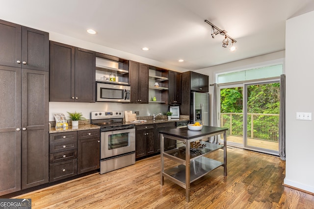 kitchen with appliances with stainless steel finishes, light hardwood / wood-style floors, light stone counters, and dark brown cabinets