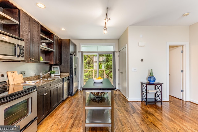 kitchen with appliances with stainless steel finishes, track lighting, dark brown cabinets, sink, and hardwood / wood-style floors